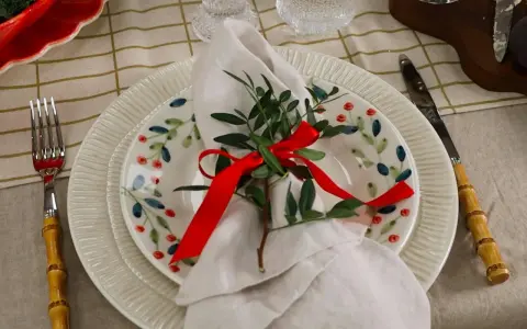 Vacker juldukning dekoration med en tallrik med bär, en vit servett med grönt och rött band, samt bestick med bambuhandtag.