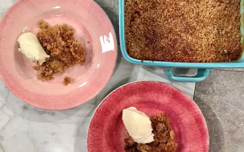 En härlig glutenfri rabarberpaj med en krispig topping, serverad med vaniljglass på rosa och röda tallrikar.
