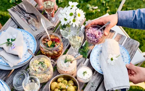 En härlig dukning med vegetarisk midsommarmat: potatissallad, sillinläggningar, gräddfil och hackad rödlök. Blommor och grönska skapar en festlig stämning.