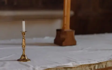 En ljusstake med ett vitt ljus står på ett vitt dukat bord. En träkorsfot skymtar i bakgrunden. Perfekt dop inspiration.