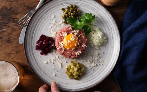 En tallrik med råbiff recept, toppad med äggula, omgiven av hackad rödbet, kapris, persilja, lök och gurka.