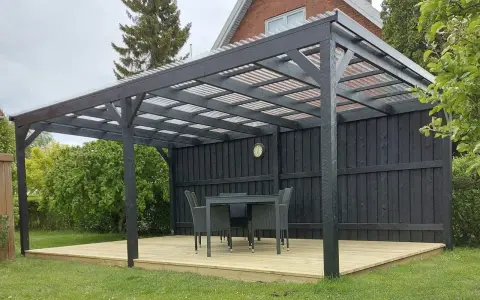 En mörk paviljong på en träaltan med bord och stolar. Perfekt för fika i trädgården.