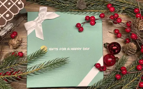 En grön presentask med texten "GIFTS FOR A HAPPY DAY", dekorerad med julgranspynt, kottar och röda bär. Perfekt för julklappar och julrim.