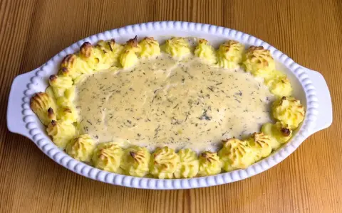 En gratinerad fiskrätt med alaska pollock recept, omgiven av spritsad potatis.