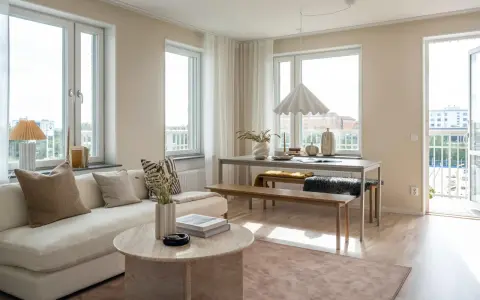 Ljust vardagsrum med soffa, soffbord och matplats. En taklampa i tyg ger ett mjukt ljus, en design klassiker som skapar atmosfär.