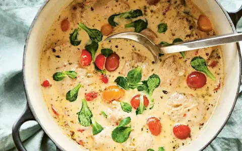 En krämig provencalsk kycklinggryta med körsbärstomater och gröna blad i en gjutjärnsgryta, redo att serveras med en slev.