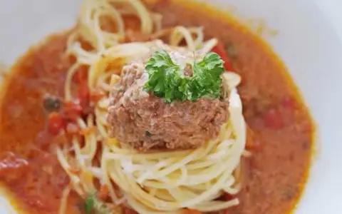 En portion spaghetti med en stor frikadell i en krämig tomatsås, toppad med färsk persilja.