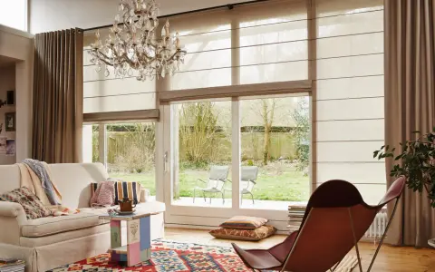 En ljus vardagsrumsmiljö med en bekväm soffa, en färgglad matta och en elegant kristallkrona. En hissgardin på gardinstång ger ett mjukt ljusinsläpp.