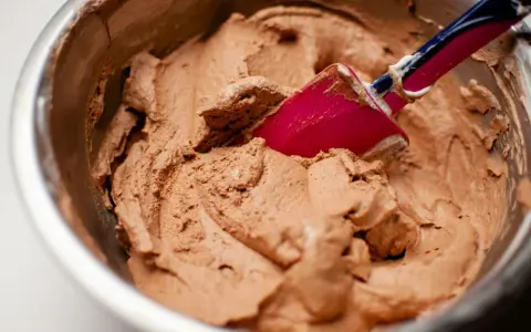 Chokladkräm i en skål, redo att bli glass. En rosa slickepott blandar i den lena smeten, kanske med lite xantangummi för perfekt konsistens.