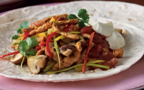 En portion fajitas med kyckling, paprika, champinjoner och lök på en tortilla, serverad med gräddfil. Ett gott fajitas recept!