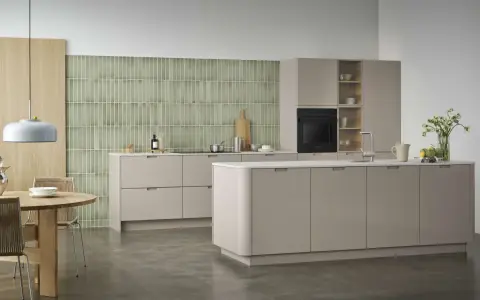 Ett modernt, hållbart kök med beige skåp, grön mosaik och ett runt matbord i trä.