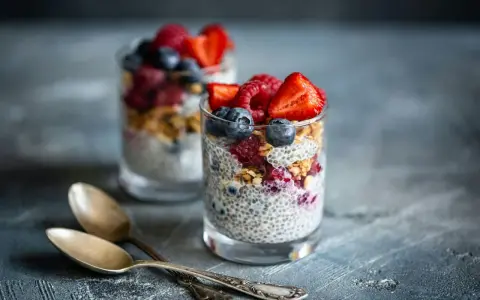Två glas med chiapudding, toppade med bär och granola. Ett perfekt chiapudding recept för en hälsosam frukost eller mellanmål.