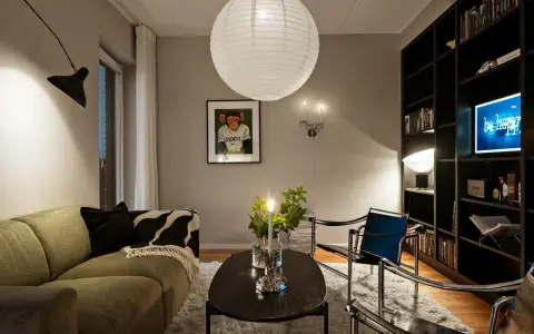 Mysig vardagsrumsmiljö med en stor papperslampa i taket. Belysning bakom gardin skapar en mjuk atmosfär.