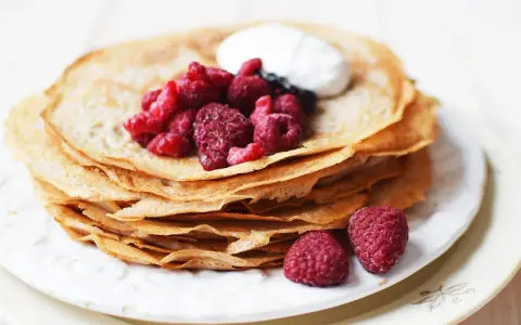 En hög med glutenfria pannkakor toppas med färska hallon och en klick grädde. Perfekt för en frukost eller fika.