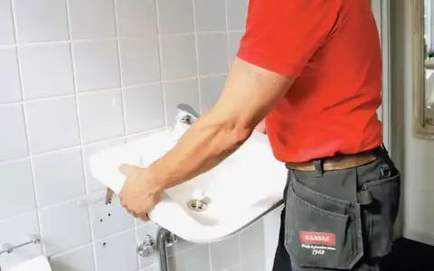 En person i röd tröja och arbetsbyxor håller i ett nytt handfat för att byta ut det gamla.