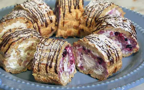 Budapestrulle recept: Skivade rulltårtor med grädde, bär och mandel, toppade med florsocker och chokladdrizzle.