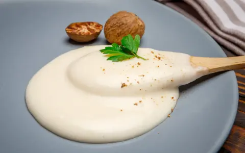 Krämig bechamelsås på en tallrik med muskotnötter och persilja. Ett enkelt bechamelsås recept för alla.