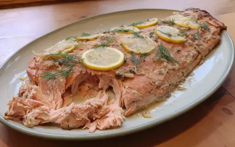 Helstekt lax i ugn, toppad med citronskivor och dill. Perfekt för en middag.