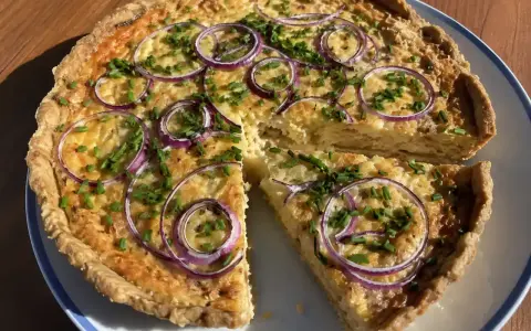 En gyllene ostpaj med rödlök och gräslök, perfekt för ett ostpaj recept. En bit är uppskuren.