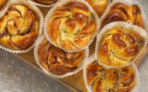 Nybakade bullar med mandelmassa, kanel och vallmofrön i pappersformar på en träbricka.