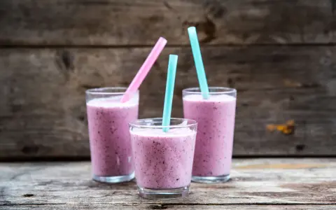Tre glas med lila smoothie, perfekta för ett snabbt smoothie recept. Blå och rosa sugrör sticker upp.