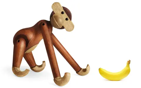 En träapa från Kay Bojesen tittar nyfiket på en banan. Olika kay bojesen apa storlekar finns tillgängliga.