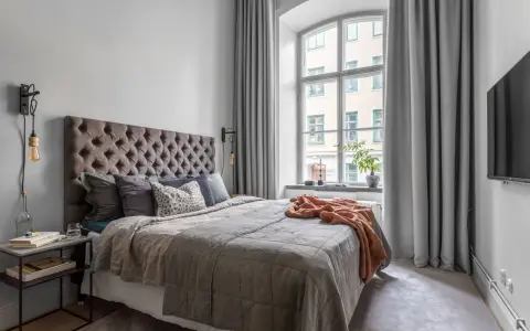 Sovrum med en stor säng, en taklampa och en **gardin på ena sidan av fönstret**.