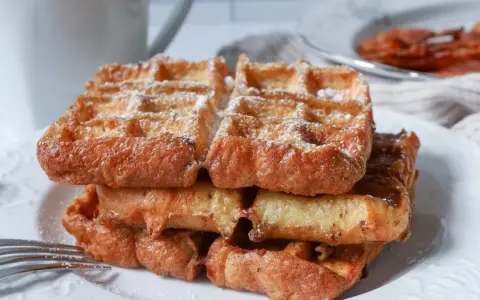 En stapel gyllene franska våfflor, pudrade med florsocker, väntar på att avnjutas. En härlig frukost eller fika.