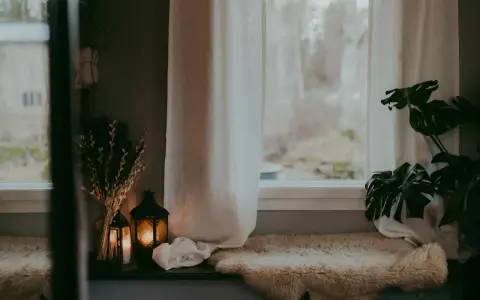 Mysig fönsterbräda med fårskinn, ljuslyktor och tunna gardiner som släpper in ett mjukt ljus.
