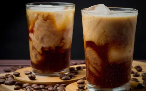 Två glas med krämigt iskaffe, perfekt för ett somrigt iskaffe recept. Kaffebönor sprider sig runt glasen.