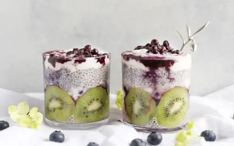 Två glas med chia pudding recept, fyllda med kiwi, yoghurt och blåbär. En vacker och hälsosam frukost.