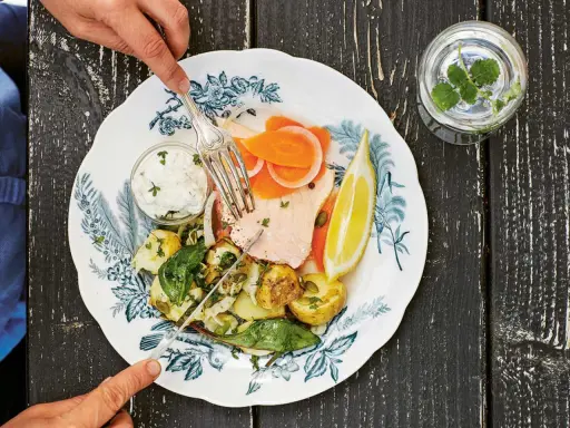En tallrik med inkokt lax, potatis, morötter, citron och en klick sås. En gaffel och kniv används för att äta.
