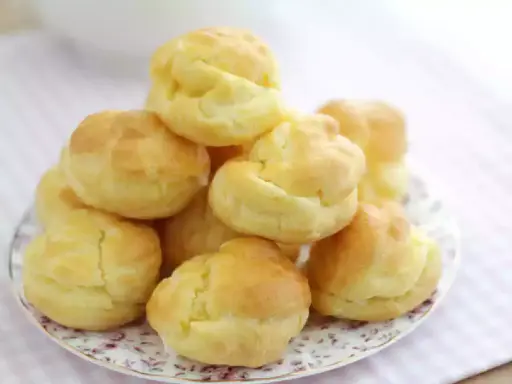 En hög med gyllene petit choux på en vacker tallrik, redo att fyllas med grädde eller glass.