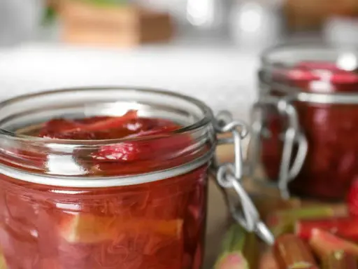 Två glasburkar med rabarberkompott, perfekt för ett gott rabarber recept. Färska rabarberstjälkar syns i förgrunden.