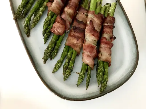 Grön sparris insvept i knaprigt bacon, serverad på en ljusblå tallrik. En läcker och enkel rätt som passar till det mesta.