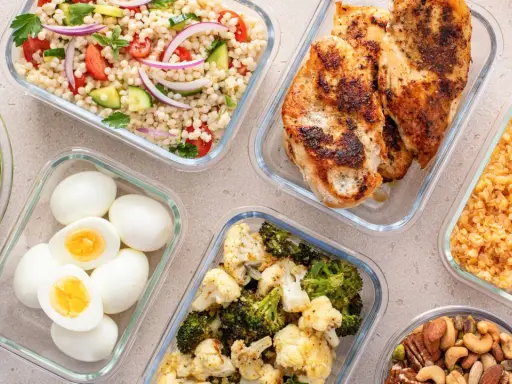 Förberedd student mat i glasbehållare: kycklingfilé, couscoussallad, grönsaker, ägg och nötter. Perfekt för en hälsosam lunchlåda.
