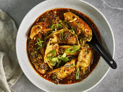 En skål med dumplings i en kryddig sås, toppad med salladslök och sesamfrön. Ett perfekt recept middag för en smakrik kväll.