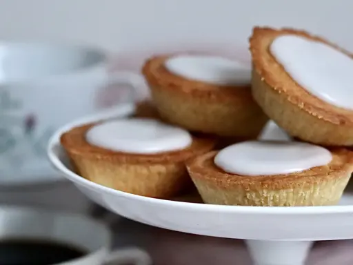 Små, gyllene mazariner med vit glasyr på ett fat. Perfekt för fikastunden, här är ett enkelt mazariner recept.