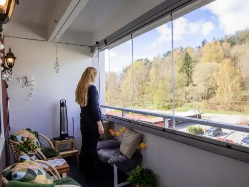 Kvinna njuter av utsikten från inglasad balkong. Mysiga sittplatser och lampor ger fina balkong tips för en ombonad känsla.