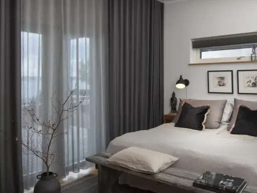 Sovrum med dubbla gardiner, ett mörkt och ett ljusare lager, som ramar in en vacker utsikt.
