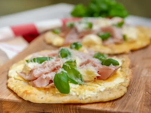 Två små pizzor med skinka, ost och basilika på en snabb pizzadeg. Serveras på en träskärbräda.
