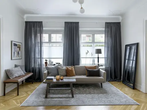 Mörka gardiner ger insynsskydd och skapar en mysig atmosfär i vardagsrummet. En bekväm soffa och en rustik soffbordsmöbel bidrar till rummets charm.