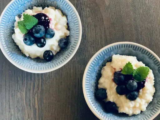 Två skålar med krämig risgrynsgröt, toppad med blåbär och mynta. Ett enkelt och gott risifrutti recept.