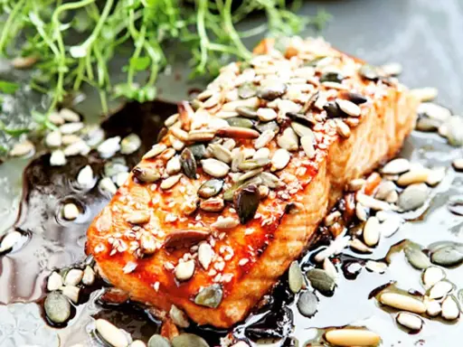 En saftig bit teriyaki lax toppad med frön, serverad i en glansig sås med gröna örter.