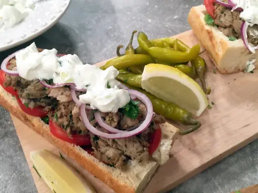En saftig gyros i baguette med tomater, rödlök och tzatziki. Serveras med pepparfrukter och citronklyfta. Ett perfekt gyros recept!