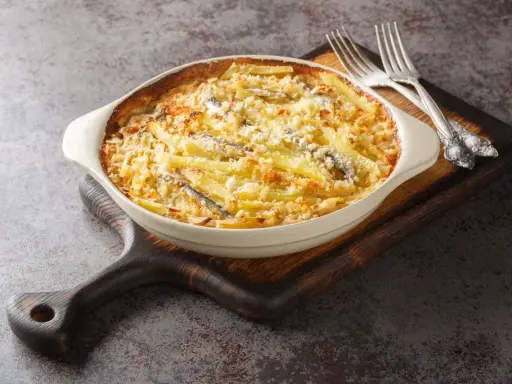 En krämig Janssons frestelse med potatis, ansjovis och ströbröd i en ugnsform, redo att serveras med två silvergafflar.