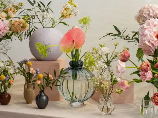 En samling vaser med olika typer av blommor, inklusive pioner, tulpaner och hortensior i mjuka pastellfärger.