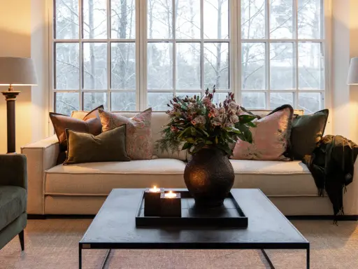 En soffgrupp med klassisk design, prydd med kuddar och en bukett blommor. Två golvlampor ger ett varmt sken.