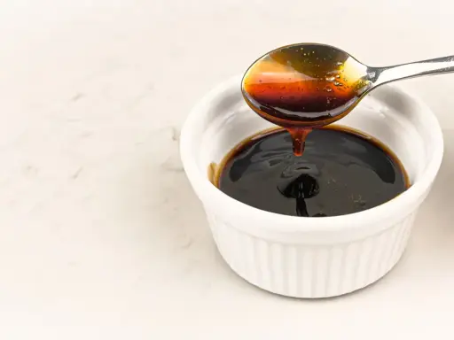 En sked häller mörk, glansig teriyakisås i en vit skål. Perfekt för ditt teriyakisås recept.