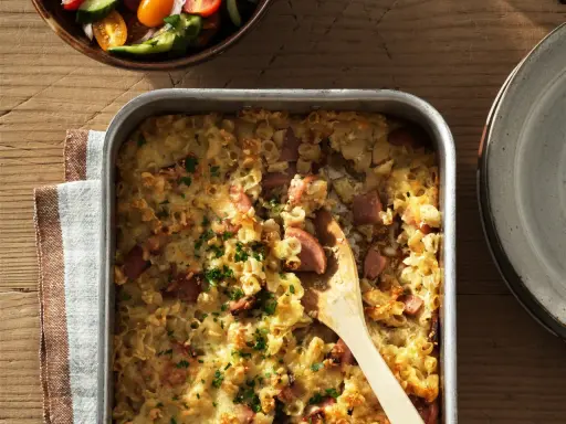 En gyllene makaronilåda med korv, toppad med persilja, redo att serveras. En klassisk svensk rätt som värmer själen.